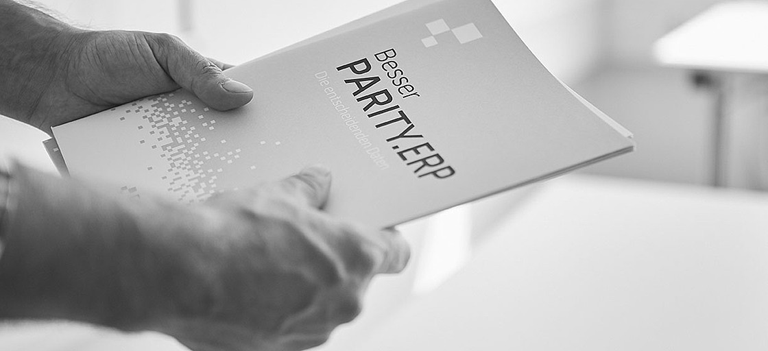 Hände halten eine Parity.ERP Broschüre mit dem Namen "Besser Parity.ERP, die entscheidenden Daten"